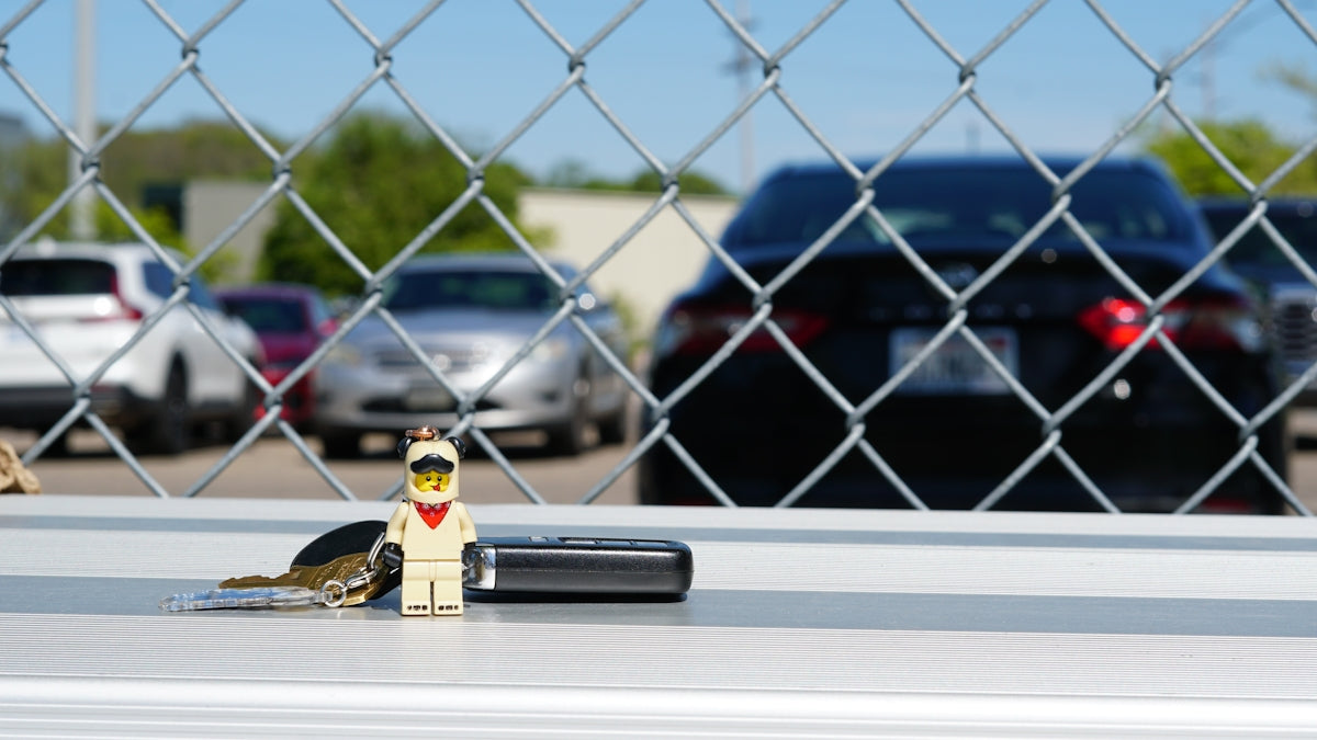 Lego chewbacca figure, keys, and remote through chain-link fence.